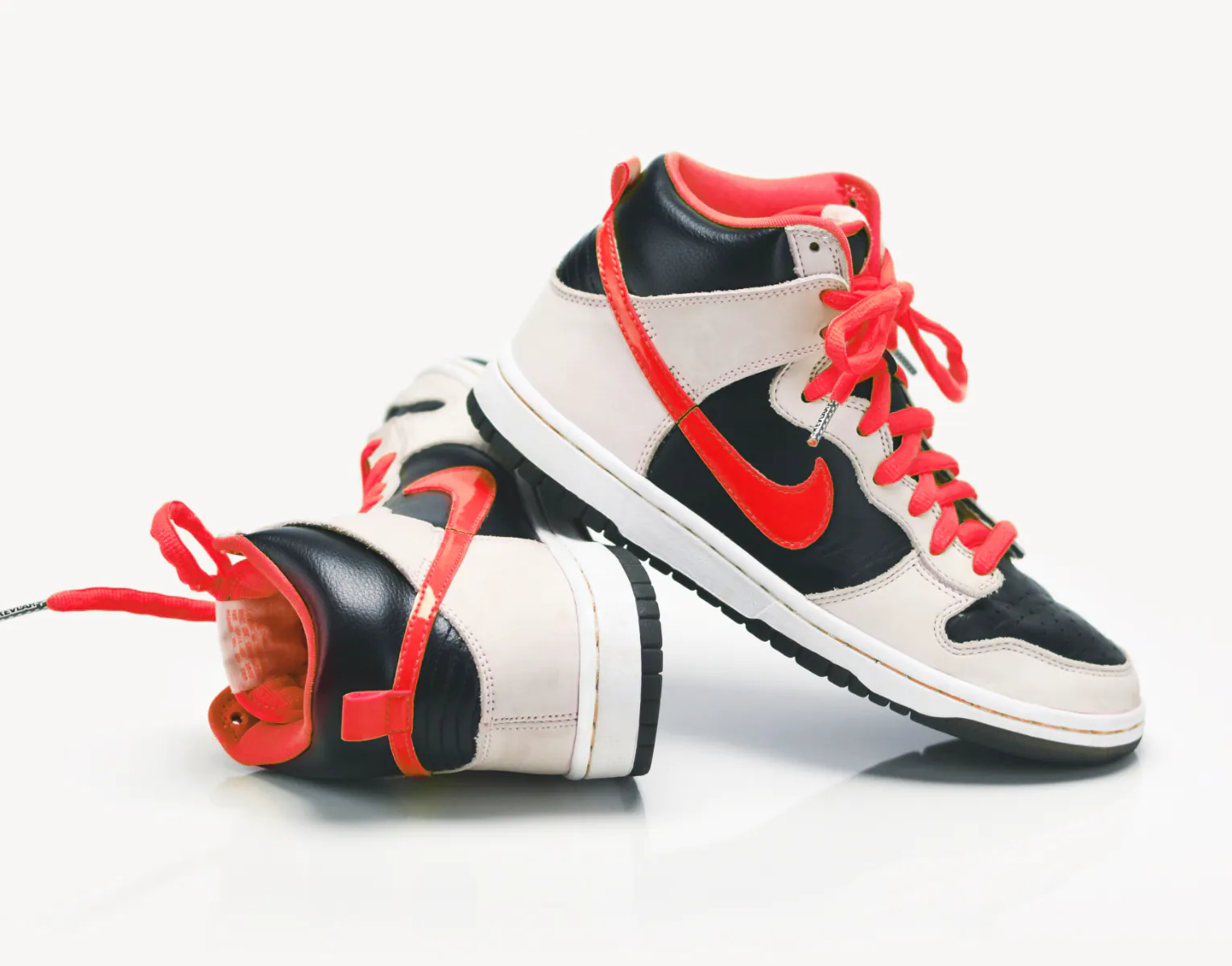 A pair of high-top sneakers with black, white, and beige panels, red accents, and red laces, placed on a white surface.