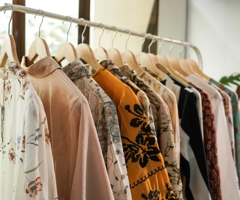 A clothing rack holding assorted long-sleeve shirts and blouses in various floral and patterned designs on wooden hangers.