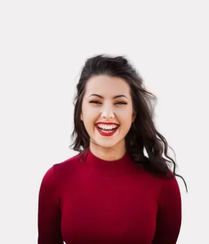 Woman with long dark hair wearing a red top is smiling widely against a plain white background.