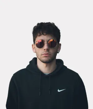 A person wearing round sunglasses and a black Nike hoodie stands against a plain white background, facing the camera with a neutral expression.