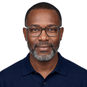 Man with short hair, beard, and glasses, wearing a dark blue collared shirt, facing forward against a plain light background.